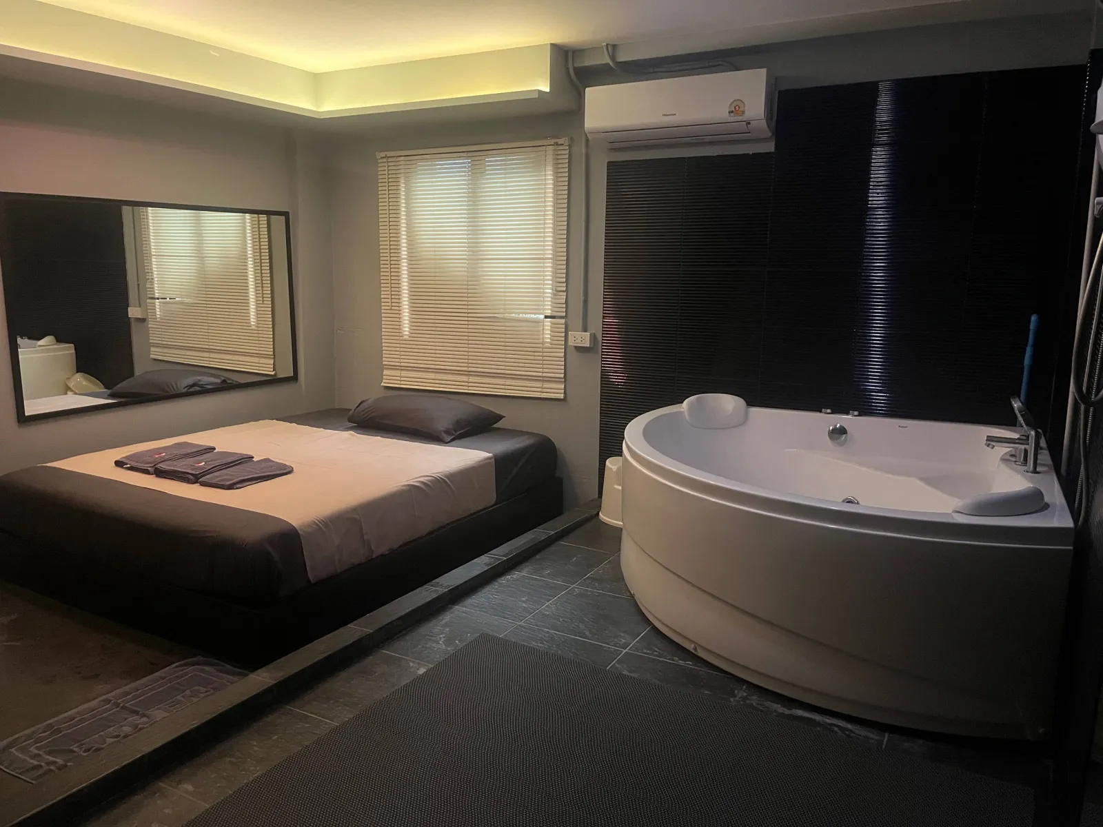 Signature suite at Heal nuru massage studio, Din Daeng Bangkok — a low massage bed beside a large round whirlpool tub, dark tile and warm light.